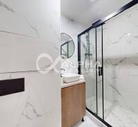 A bathroom in a 2-room apartment with marble tiles and a glass shower enclosure.