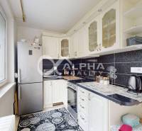 Kitchen of a 2-room apartment with light cabinets, black tiles, and a view from the window.