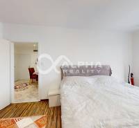 A bedroom in a two-room apartment with a wood-patterned floor and a large window.