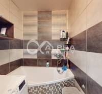 A bathroom with a bathtub in a 2-room apartment, tiled with ceramic tiles and a shower faucet.