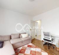 A room in a 2-room apartment with a corner sofa, a floor with a wood decor, and a desk.