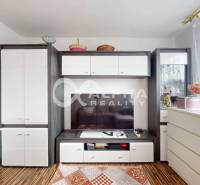 Living room in a two-room apartment with a television, white furniture, and a wooden decor floor.