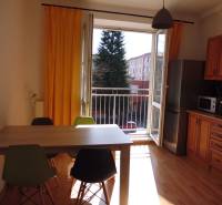 A kitchen in a studio apartment with furniture, yellow curtains, and a wooden decor floor.