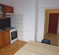 A kitchen in a studio apartment with a simple kitchenette and a floor with a wood decor.