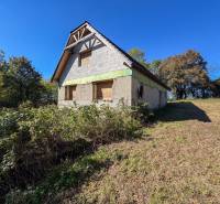 An unfinished building on agricultural and forest land in Lackov, surrounded by green trees and grass.