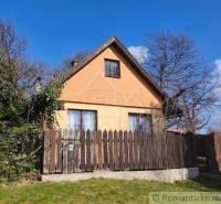 A cottage in Hronská Dúbrava surrounded by greenery and a wooden fence, with a clear blue sky.