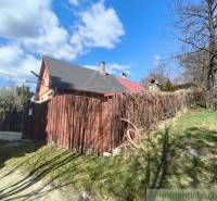 A cottage in Hronská Dúbrava with a garden, wooden fence, and blue sky.