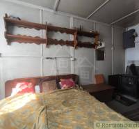 A bedroom in a cottage with simple furniture and a wood stove.