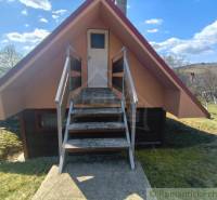 A cottage in Hronská Dúbrava with wooden stairs, surrounding trees, and a clear sky.