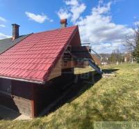 A cottage in Hronská Dúbrava with a staircase and a red roof on a vast meadow.