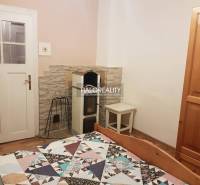 In the family house, there is a room with a stove, a bed, a cabinet, and a floor with a wooden decor.