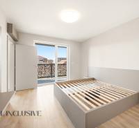 A bright bedroom with a bed and a balcony in a 2-room apartment, with a wooden decor floor.