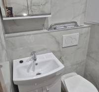 A bathroom in a studio apartment with a sink, mirror, and toilet, tiled with light tiles.