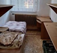 A narrow room with a bed, storage space, and wooden floor decor in a family house.