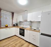 A kitchen with white cabinets, wood-patterned flooring, and modern appliances in a three-room apartment.