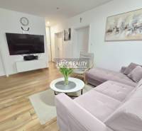 A kitchen and dining room in a three-room apartment with a wood-patterned floor and a pink sofa.