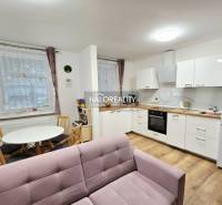 Living room with a pink sofa, kitchen, and wooden decor flooring in a three-room apartment.
