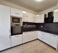 A kitchen with white cabinets, black appliances, and a wood-patterned floor in a three-room apartment.