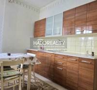 A kitchen in a family house, equipped with a dining table, chairs, and windows with white curtains.