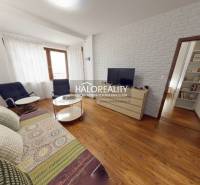 Living room with a sofa, TV, and wood-patterned flooring in a three-room apartment.