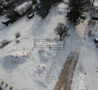Snow-covered residential lands in Liptovské Beharovce surrounded by trees and buildings.