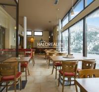 A hotel restaurant with a glass wall, overlooking snow-covered mountains and forests.