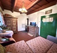 Rustic interior of a cottage with wooden beams, antique furniture, and green doors.