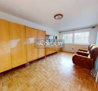 A room with furniture and a wooden decor floor in a family house, illuminated by large windows.