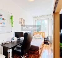 A room in a 3-room apartment with a wooden decor floor, a desk, and a bed.