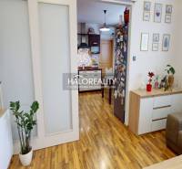 Living room of a two-room apartment with a wooden decor floor and a kitchen in the background.