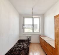 A bedroom in a two-room apartment with a window, a simple bed, and a wooden wardrobe.