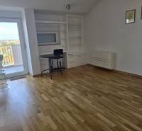Interior of a vacation apartment with wood-patterned flooring, a table, and built-in shelves.
