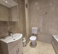 A bathroom in a holiday apartment with sanitary ware and tiles in neutral tones.