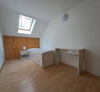 A bright room with a bed, a desk, a skylight, and a wooden floor.