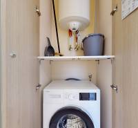 Storage space with a washing machine in a 3-room apartment, shelves, boiler, broom, and bucket.