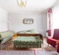 A room in a family house with two beds, carpets, and armchairs under the window.