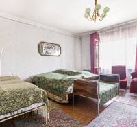 A room in a family house with three beds, carpets, and a large window with curtains.