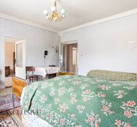 A room in a family house with beds, floral blankets, and antique furniture.