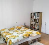 Bedroom in a 2-room apartment with a bed, floral bed linens, and a bookshelf.