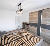 Bedroom in a two-room apartment with a wood-patterned floor and wardrobes with sliding doors.
