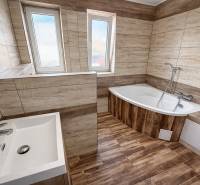 Bathroom in a two-room apartment with a wooden-patterned floor and a corner bathtub.