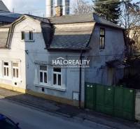 A family house in Rimavská Sobota with a classic roof design, a large gate, and neighboring buildings.