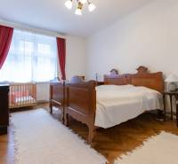 A bedroom in a three-room apartment with a wooden decor floor, a crib, and red curtains.