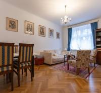 Living room with a sofa, bookshelf, chairs, wooden decor flooring, and a chandelier in a three-room apartment.