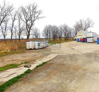 In the yard, storage containers, waste bins, background with bare trees and offices.