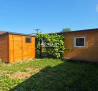 Wooden garden houses in the Gardens of Bojnice, surrounded by greenery and blue sky.