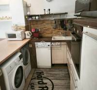 A kitchen in a 2-room apartment with a washing machine, microwave, and kitchen units.