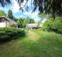 A green plot with a cottage and trees in Starý Huta under a blue sky.
