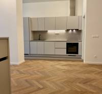 A kitchen in a 2-room apartment with a wood-patterned floor and light cabinets.