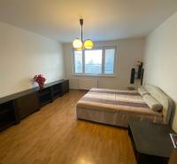 A room in a three-room apartment with a bed, dark furniture, and a floor with a wood decor.